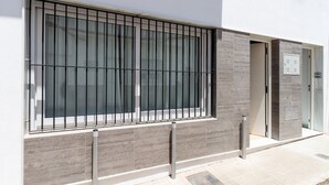 Une façade d’immeuble avec une fenêtre grillagée, un poste de sécurité en métal et une entrée carrelée.