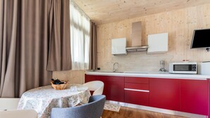 A compact kitchen with wooden walls, a red countertop, a white microwave, and a dining area with a table and chairs. - With panoramic views in the hills – Apartment GeoResort A2 (Tremosine sul Garda)