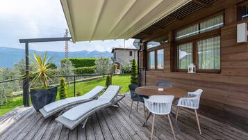 Eine Holzterrasse mit Liegestühlen, einem Tisch und Stühlen mit Blick auf eine gebirgige Landschaft.