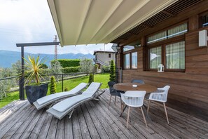 Una terraza de madera con sillones de descanso, una mesa y sillas, con vistas a un paisaje montañoso.