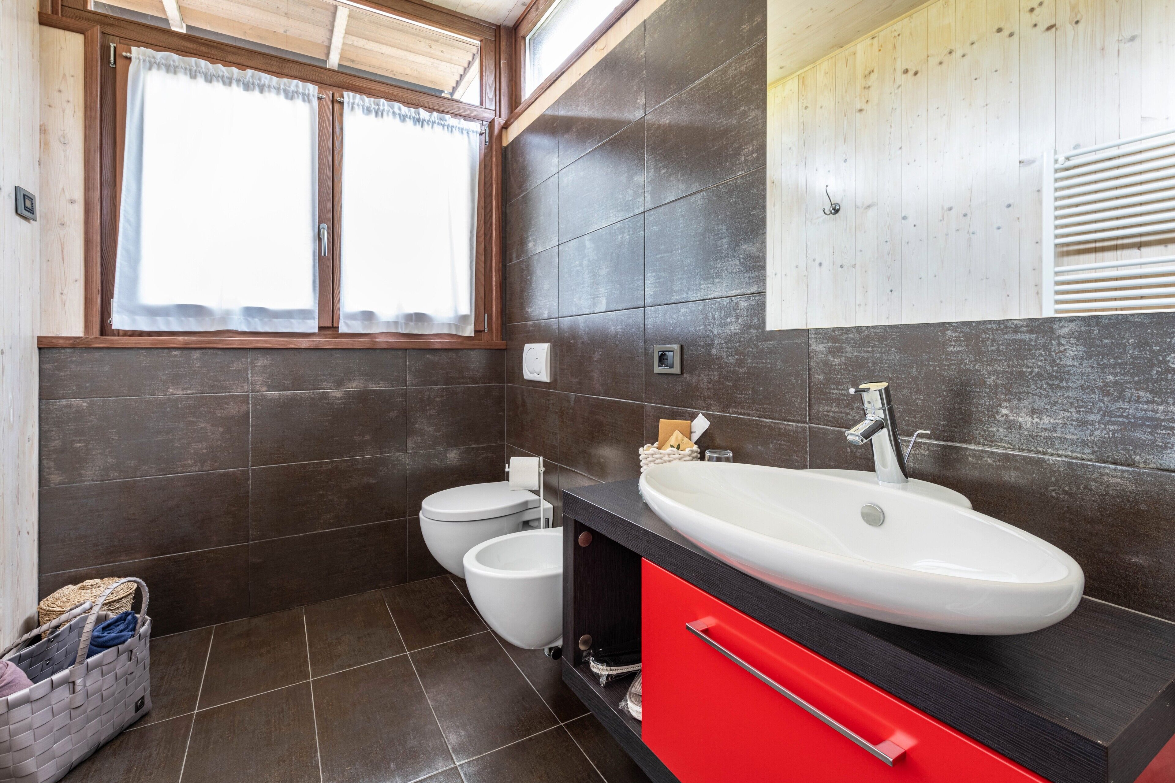 Un bagno moderno con un lavandino ampio, due servizi igienici e una finestra con tende.