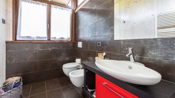 Un bagno moderno con un lavandino ampio, due servizi igienici e una finestra con tende.
