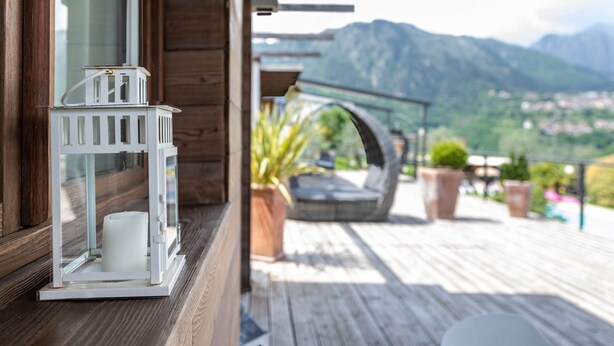 A wooden deck with a white lantern, a potted plant, and a view of mountains. - With panoramic views in the hills – Apartment GeoResort A2 (Tremosine sul Garda)
