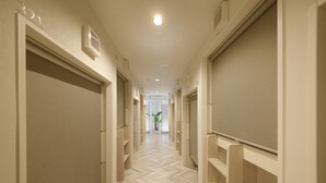 A hallway with a herringbone floor pattern, white walls, and a potted plant in the distance. - Lestel Maru - Hostel (Sapporo)