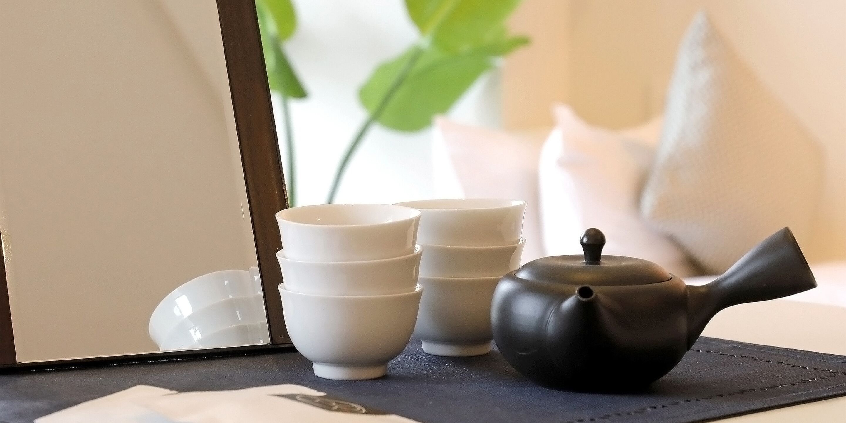 A stack of white bowls and a black teapot on a table with a placemat.