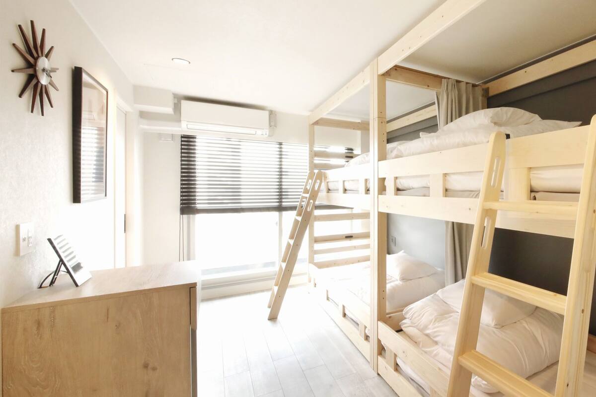 A bunk bed room with a desk, a ladder, and a window with blinds.