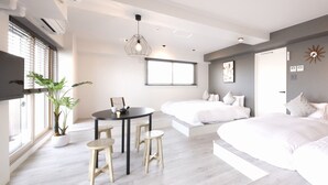A modern bedroom with a large bed, a smaller bed, a dining area with stools, and a potted plant. - Lestel Maru - Hostel (Sapporo)