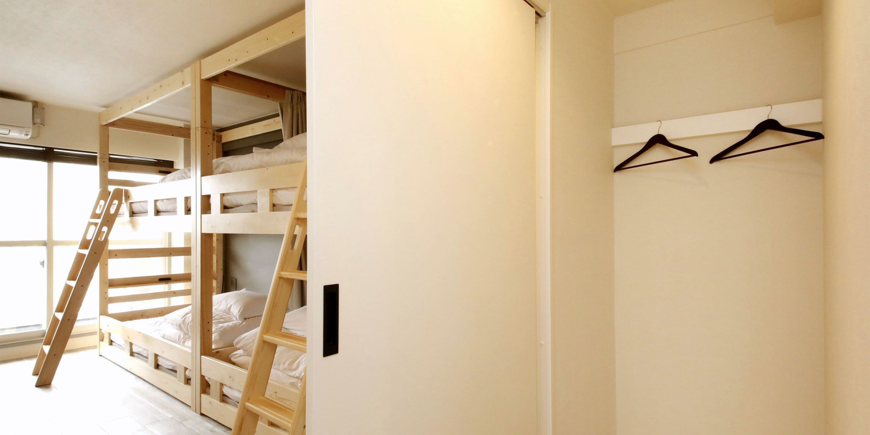 A bunk bed room with a ladder, a window, and a wall-mounted hanger.