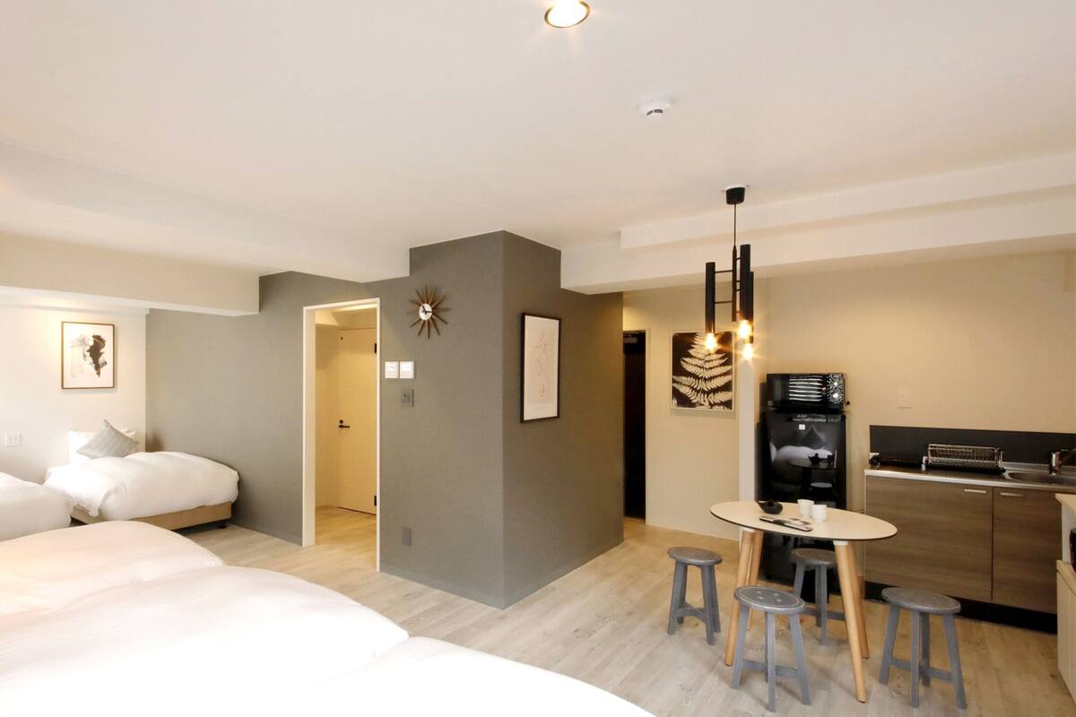 A modern hotel room with a large bed, a small dining area, and a kitchenette.