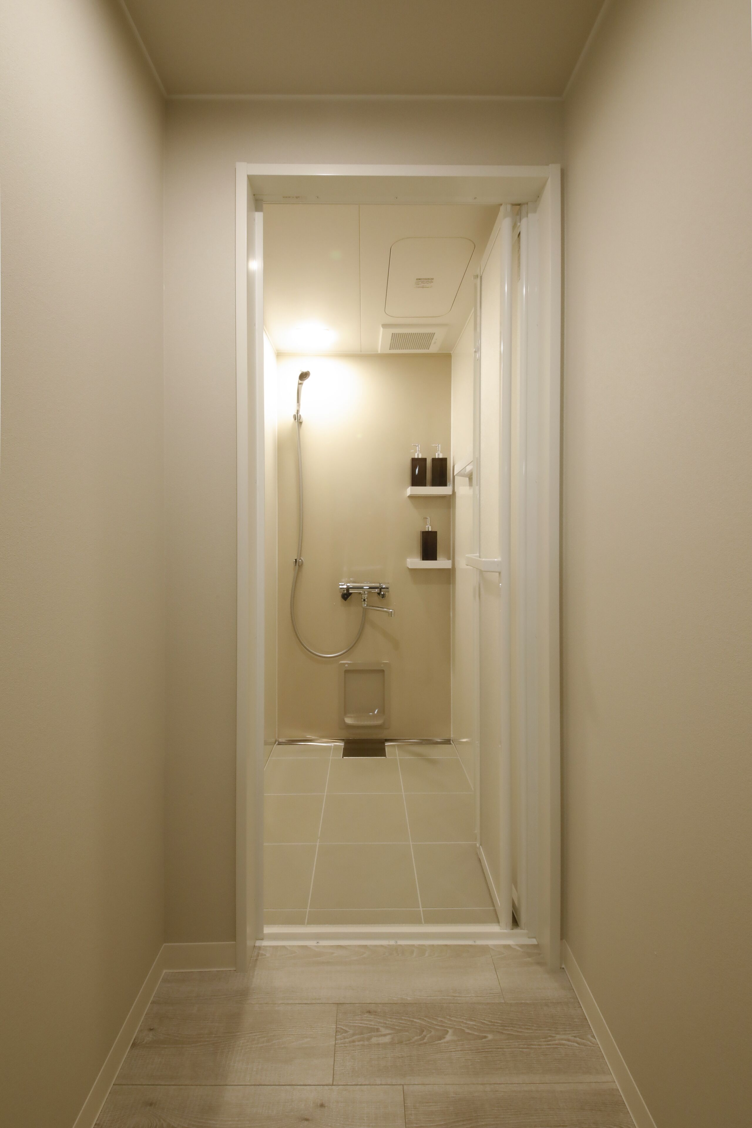 Un corridoio stretto che porta a un bagno con doccia, toilette e mensole con articoli da toilette.