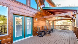 Una terraza de madera con zona cubierta, mobiliario exterior y una puerta con ventanal.
