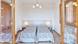 Ein Schlafzimmer mit zwei Betten, einer Kandelaber, Nachttischen und Blick durch eine Glastür.