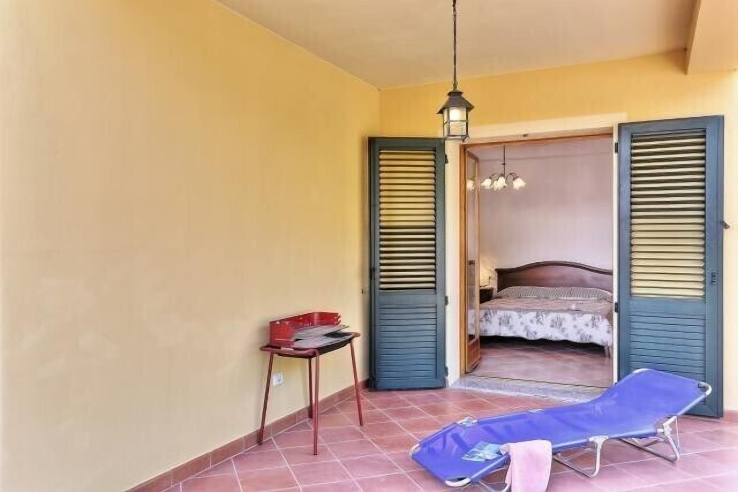 A room with a bed, a table with a red basket, a blue chair, and a hanging light fixture.