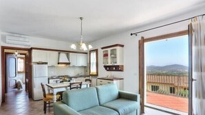 Ein Wohnzimmer mit einer Couch, einem Esstisch mit Stühlen, einer Küchenzeile und einem Balkon mit Blick.
