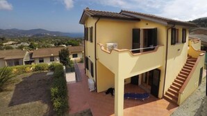 Ein zweistöckiges Haus mit Balkon, Treppe und Blick auf die umliegende Landschaft.