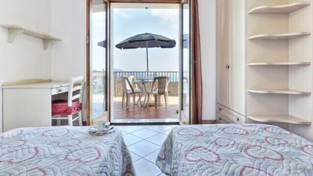 Ein Zimmer mit zwei Betten, einem Balkon mit Tisch und Stühlen sowie Blick aufs Meer.