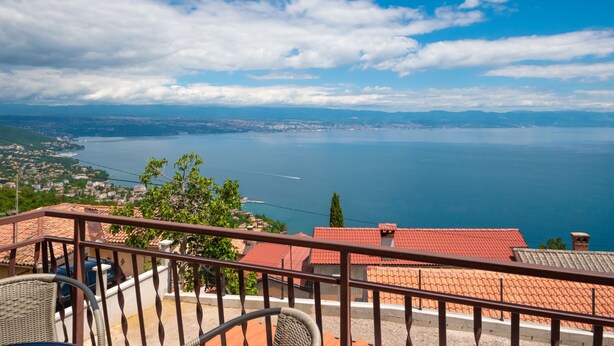 Un balcon offrant une vue sur un paysage urbain côtier, comprenant une étendue d’eau et des montagnes lointaines.
