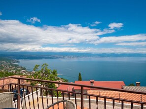 Un balcón con vistas a una ciudad costera, incluyendo una masa de agua y montañas distantes.