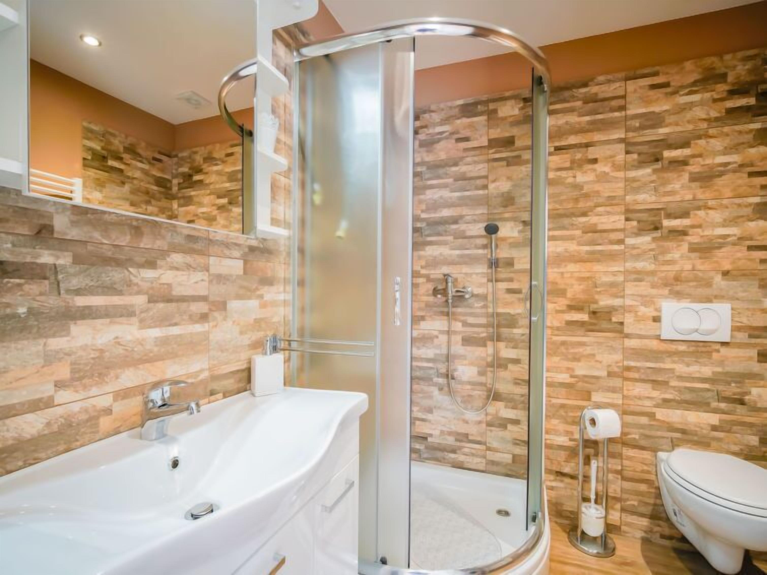 Ein modernes Badezimmer mit einer gläsernen Duschkabine, einer weißen Badewanne und einer Toilette.