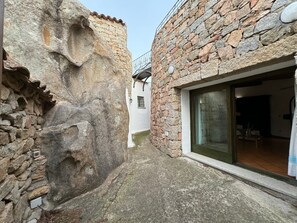 A stone building with a large rock formation, a white exterior, and a glass door leading to an interior space.