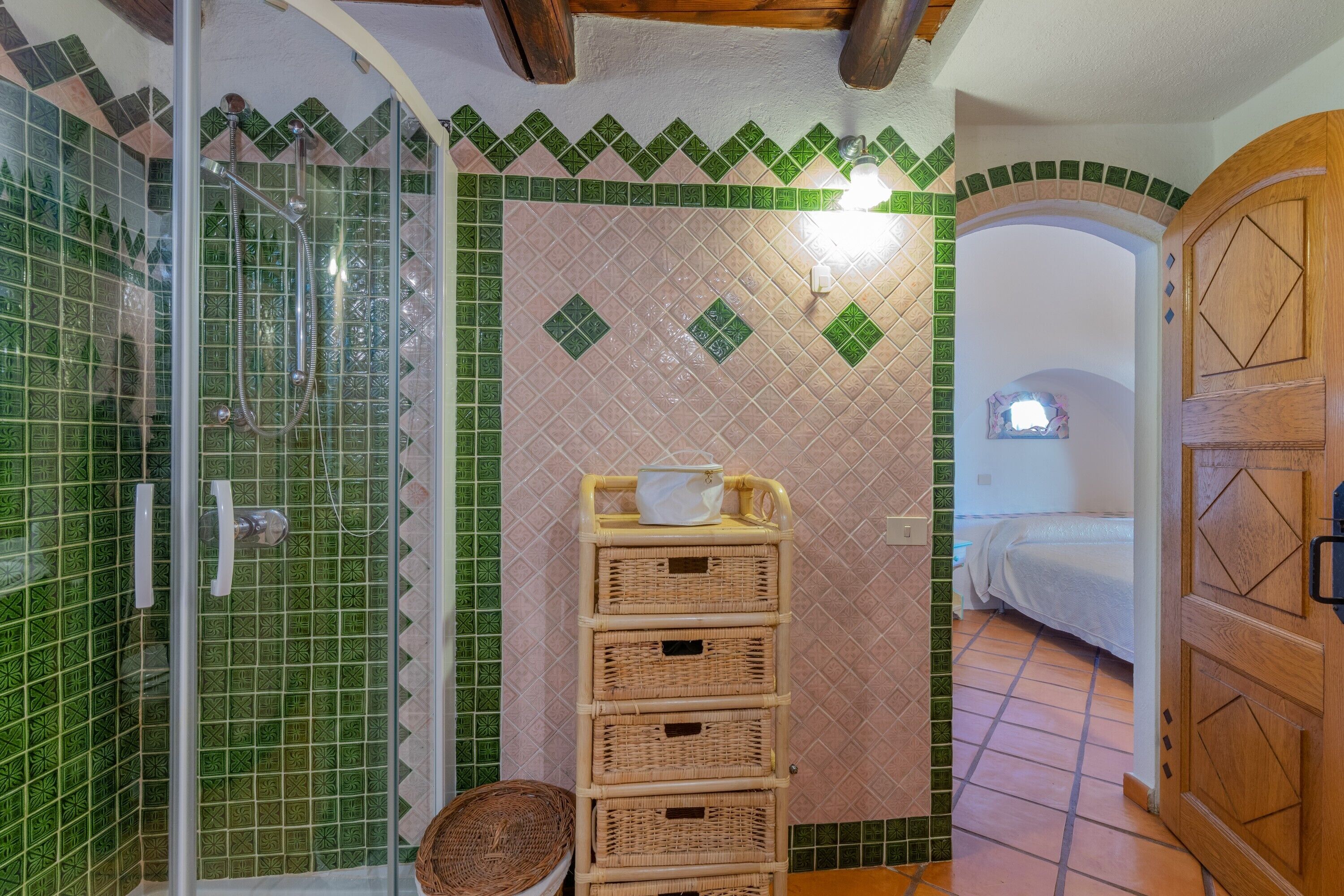 Une salle de bain avec une douche, un lavabo et un lit visible à travers une porte ouverte.