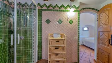 Une salle de bain avec une douche, un lavabo et un lit visible à travers une porte ouverte.