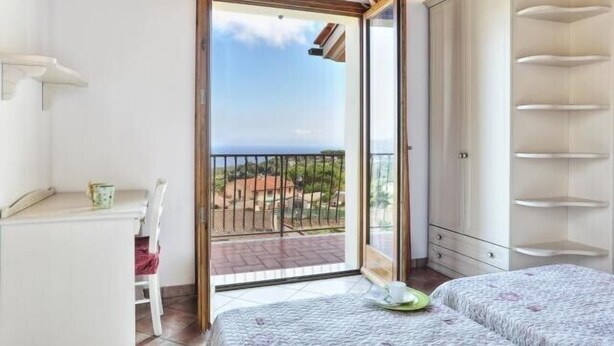 Ein Schlafzimmer mit Balkon, einem Bett, einem Sessel und einem Kleiderschrank.