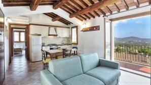 Eine moderne Küche mit weißen Schränken, ein Essbereich mit Tisch und Stühlen sowie ein Balkon mit Blick auf die Landschaft.