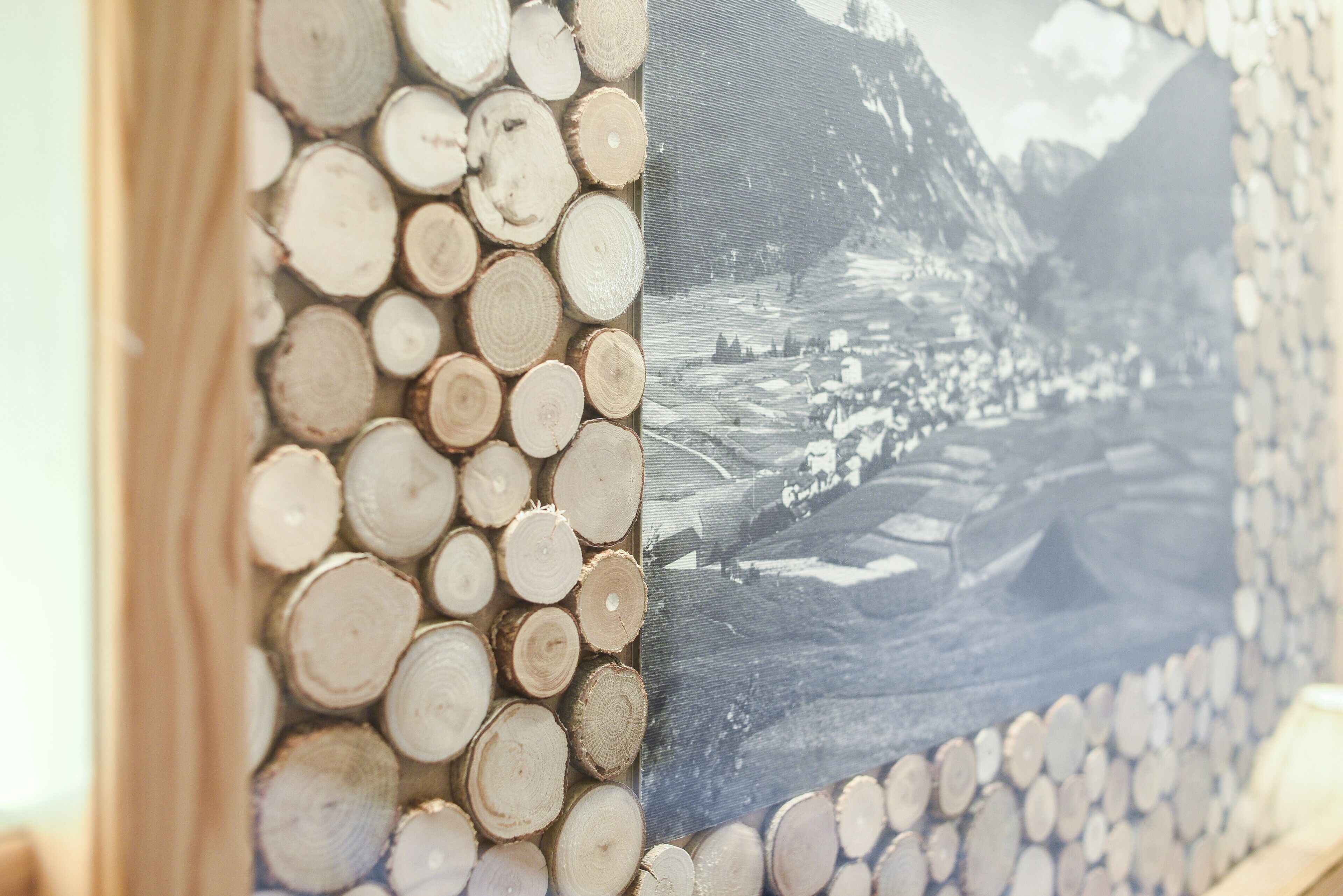 Un primo piano di un muro con un motivo di tronchi di legno circolari e una fotografia di un paesaggio montano.