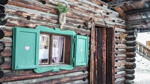Une cabane rustique en rondins de bois, dotée d’une fenêtre ornée de découpes en forme de cœur, d’un banc en bois et d’un escalier en bois.