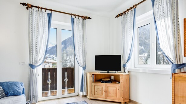 Une chambre à coucher avec un lit, un téléviseur posé sur un meuble en bois, et une vue sur une montagne enneigée à travers une porte vitrée.