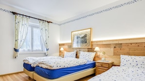 Une chambre avec deux lits, une tête de lit en bois, une table de chevet avec une lampe et une fenêtre avec des rideaux.