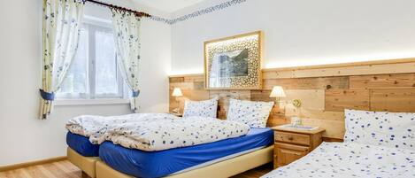 A bedroom with two beds, a wooden headboard, a bedside table with a lamp, and a window with curtains.