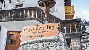 Une enseigne en bois indiquant « Ciasa Cristina Apartments » et « Ferienwohnungen », ce qui désigne un hôtel ou un complexe d’appartements.