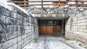 Un couloir aux murs de pierre, avec une porte en bois et un escalier en pierre menant à l’étage supérieur.