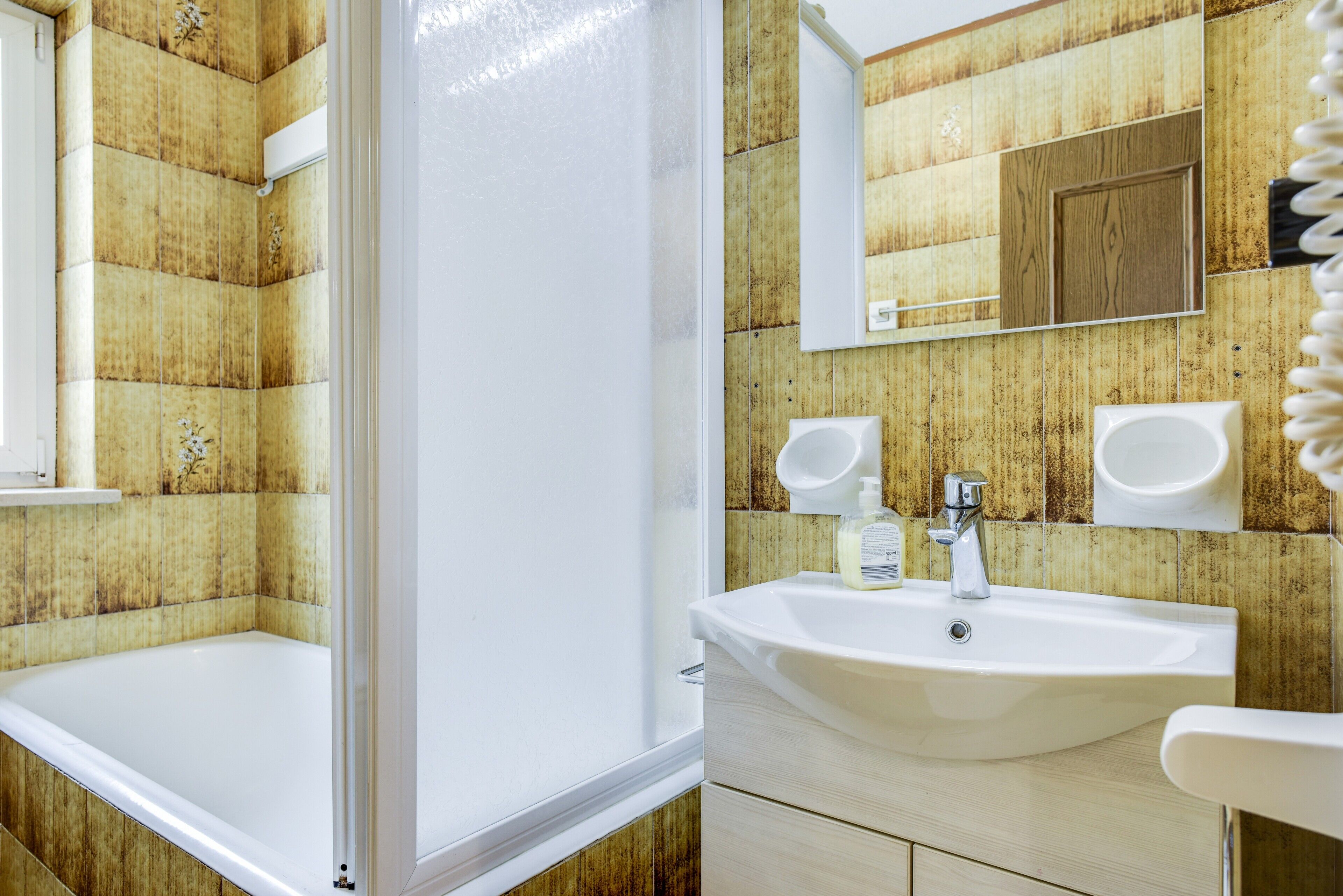 Une salle de bain avec une baignoire, un lavabo, un miroir et des murs recouverts de lambris en bois.