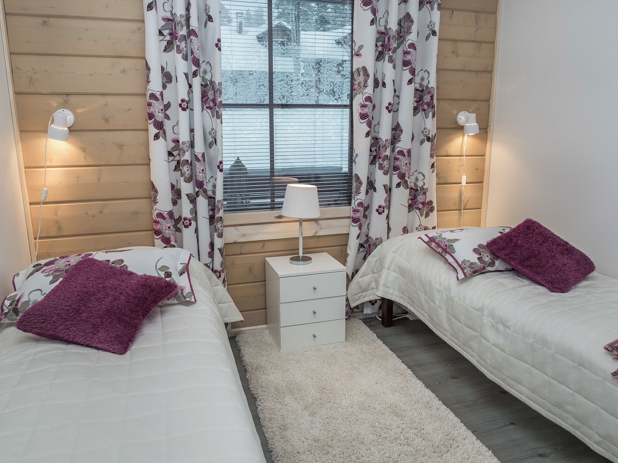 Een slaapkamer met twee bedden, een nachtkastje, een lamp en een raam met gordijnen.