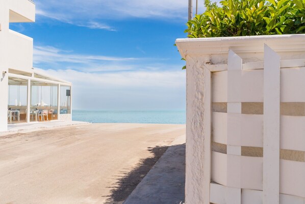 A beachfront property with a patio, a white building, and a view of the sea.