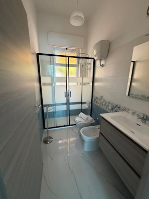 Ein modernes Badezimmer mit einer Duschkabine aus Glas, Toilette, Bidet und Waschtisch mit Spiegel.