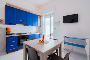 A modern kitchen with blue cabinets, a dining table, and a TV mounted on the wall.