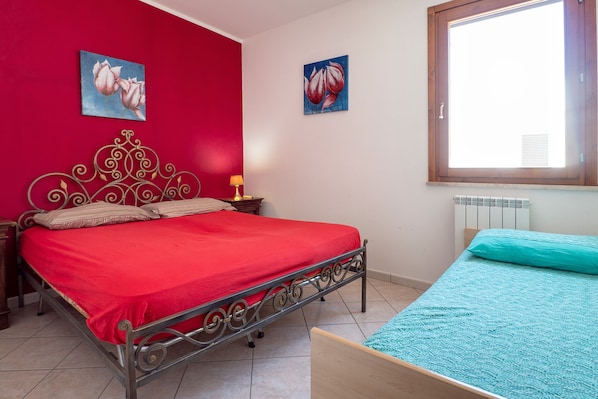 A bedroom with a metal bed frame, a red wall, and a window with blinds.