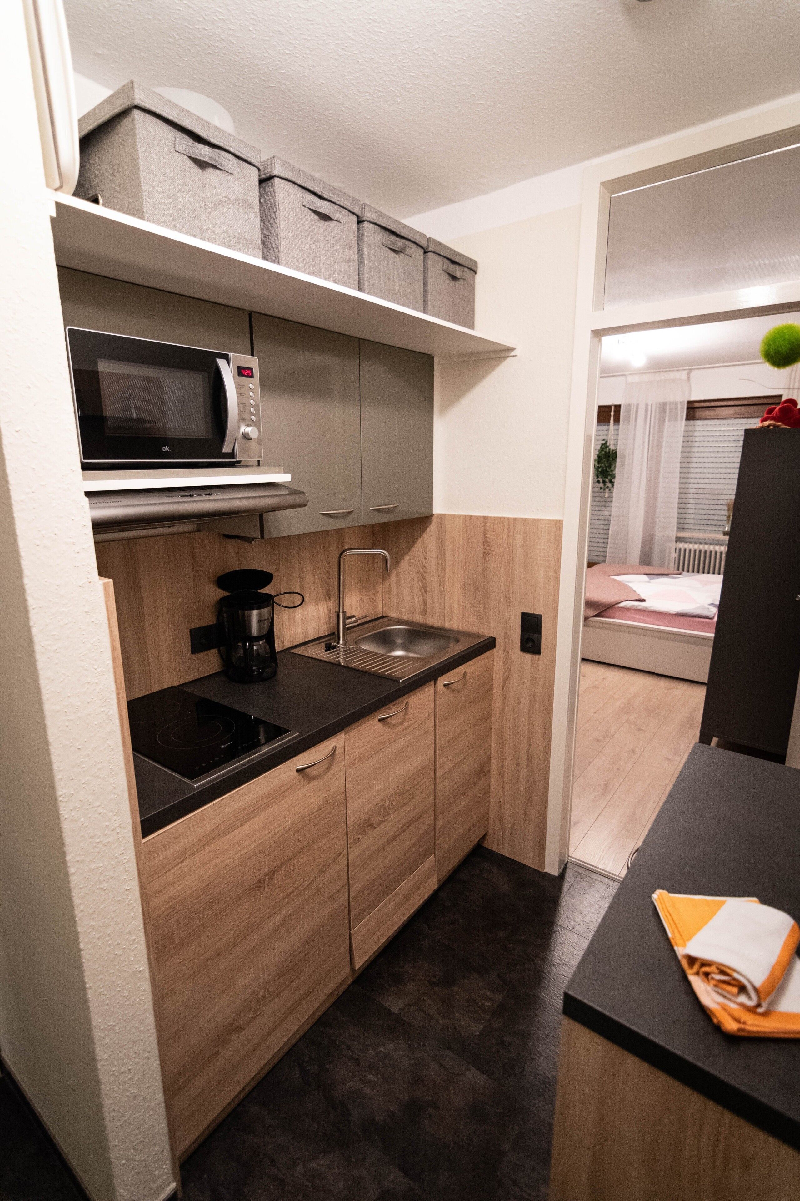 Una cocina compacta con microondas, cafetera y armarios de madera.