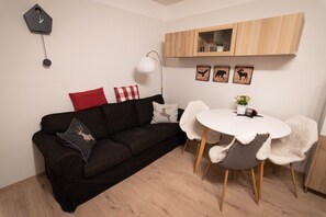 Ein modernes Wohnzimmer mit einer schwarzen Couch, einem runden weißen Tisch und einem Holzschrank darüber.