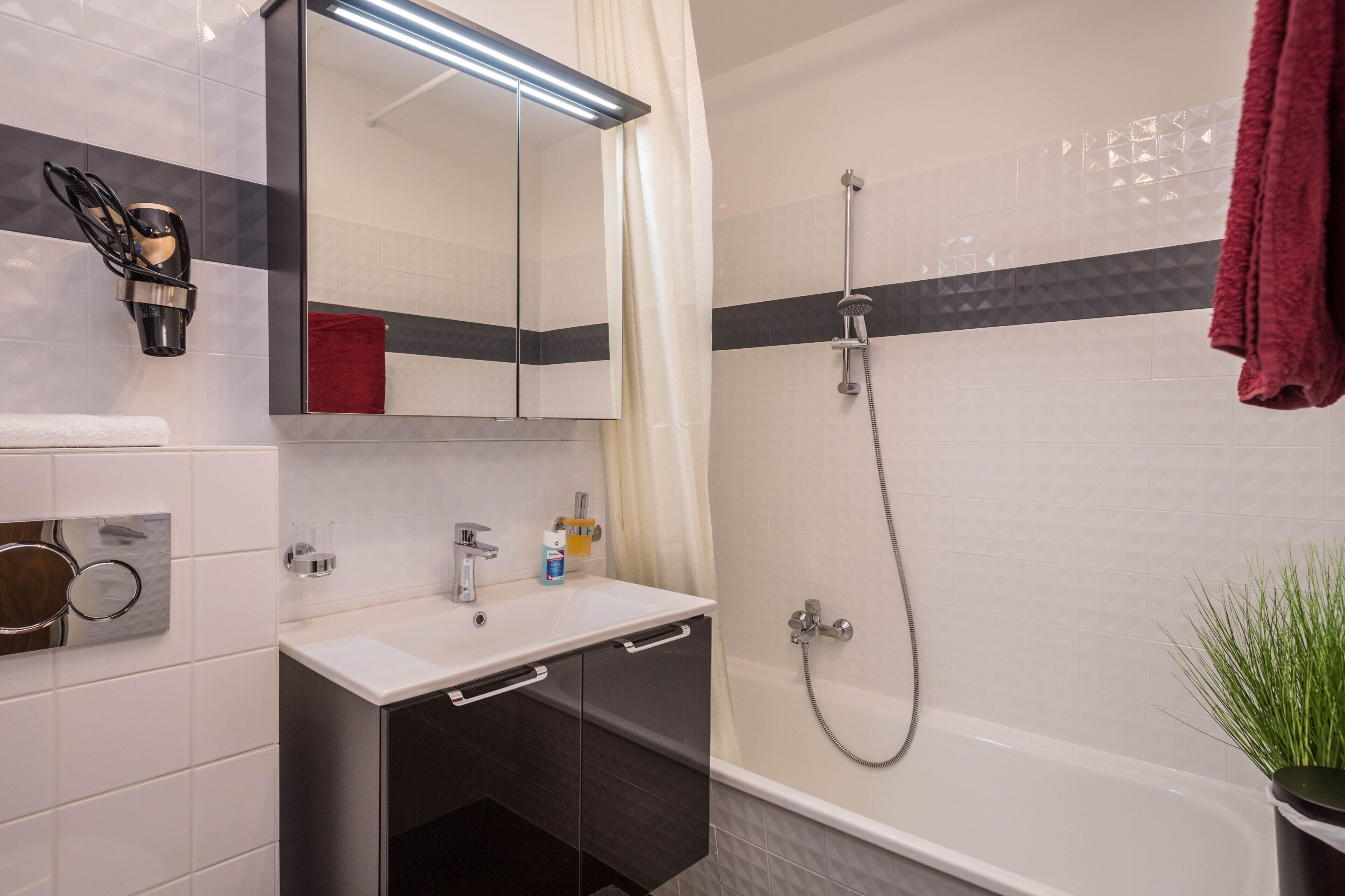 A bathroom with a white sink, a mirror, a shower, and a red towel.