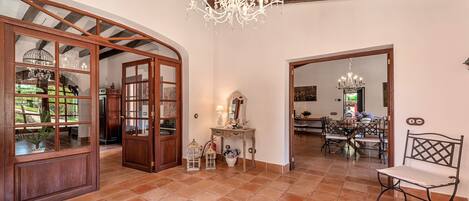 A spacious room with a large wooden door, a chandelier, and a dining area with chairs and a table.