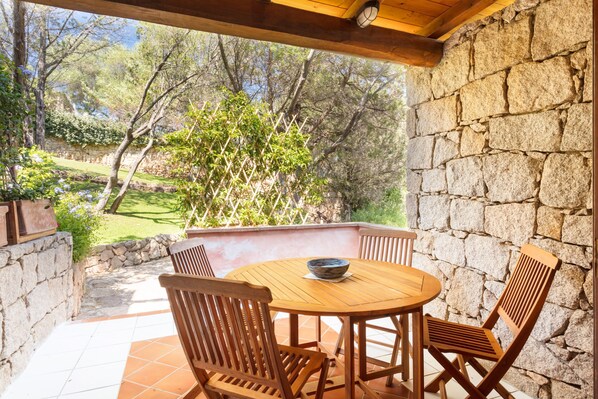 Un patio con una mesa y sillas de madera redonda, una pared de piedra y vistas a un jardín.