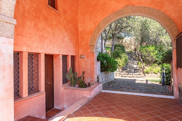 Uma entrada em arco para um edifício com um pátio pavimentado, uma escadaria de pedra e uma planta de cacto.