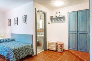 Un dormitorio con cama, un baño visible a través de una puerta abierta, un armario blanco pequeño y un guardarropa azul.