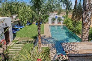 A swimming pool with a clear blue water, surrounded by a well-maintained lawn and various plants. - Charming Apartment with Pool, Terrace, Air Conditioning and Wi-Fi (Conil)