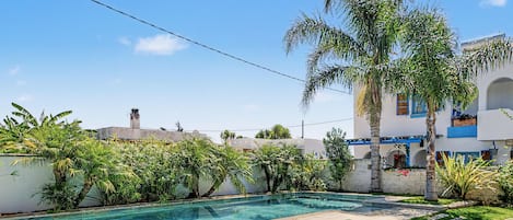 A swimming pool surrounded by lush greenery and a white building with blue accents.